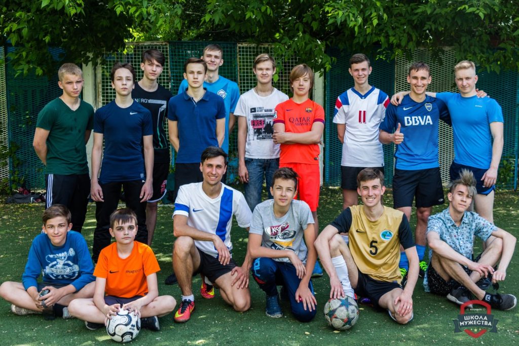 Команда мальчиков «Школы мужества» с тренерами и мячами на футбольном поле
